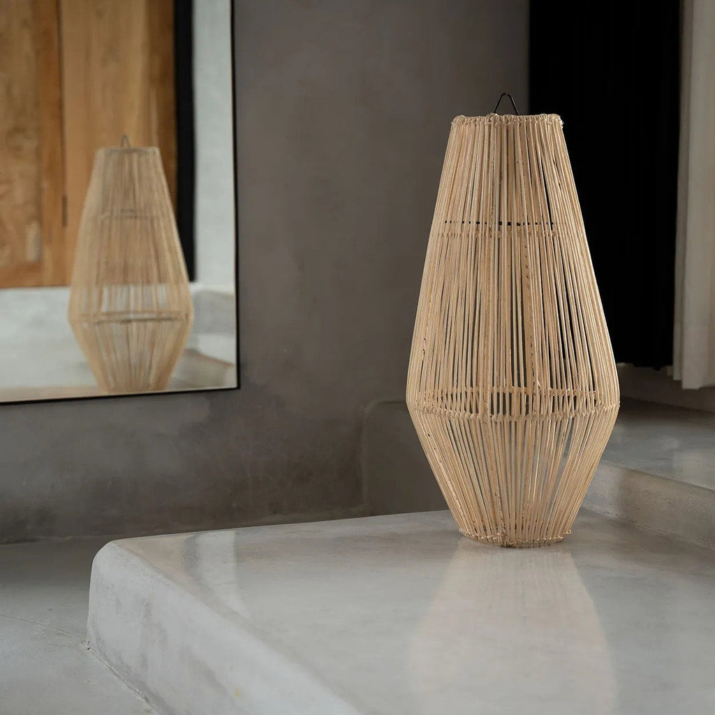 Woven rattan vase on a reflective surface with a neutral background