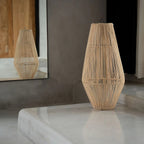 Woven rattan vase on a reflective surface with a neutral background