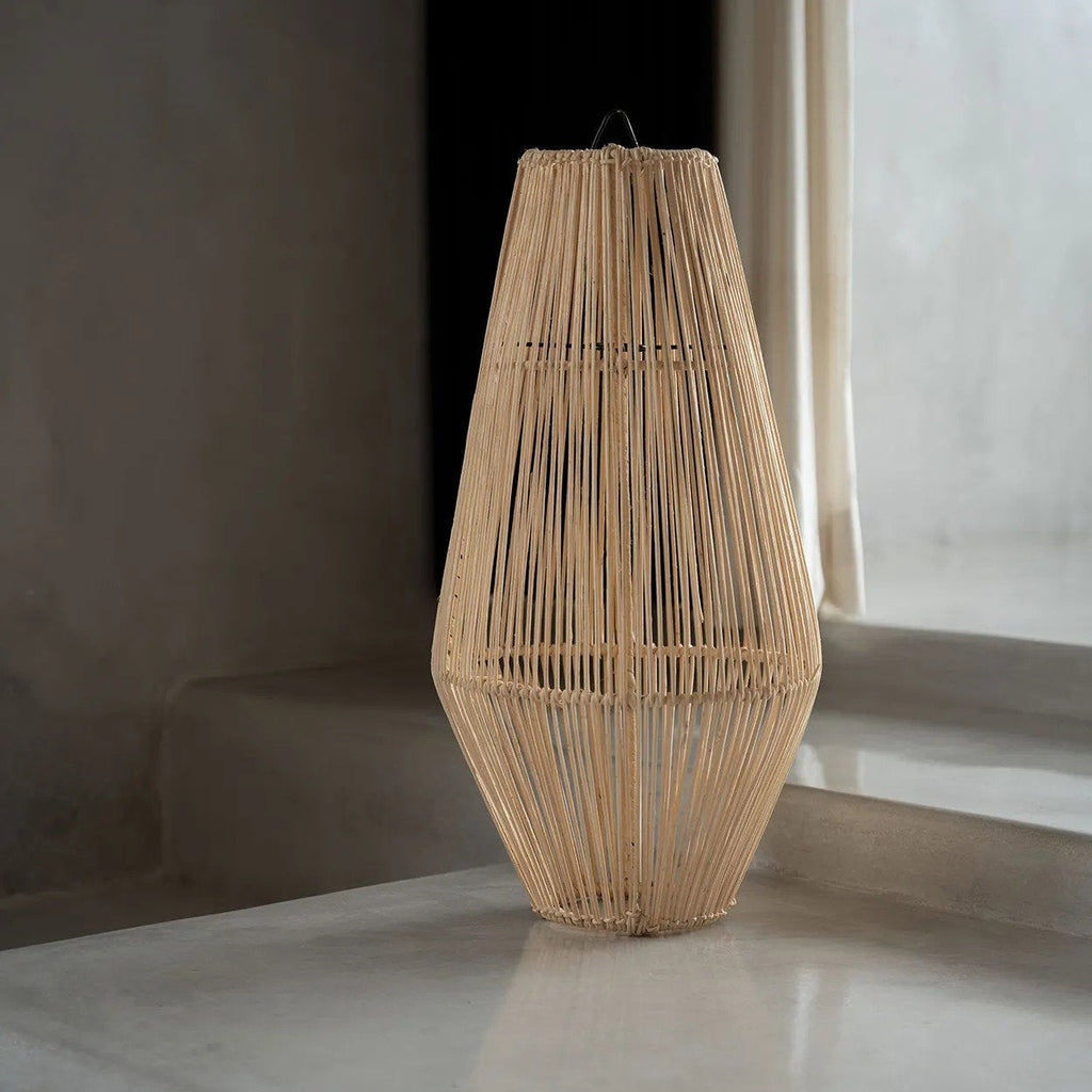Woven rattan lamp on a reflective surface with a neutral background