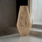 Woven rattan lamp on a reflective surface with a neutral background